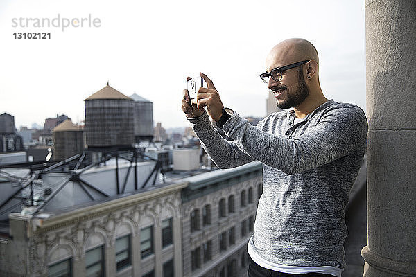 Lächelnder Mann fotografiert mit Smartphone auf dem Balkon