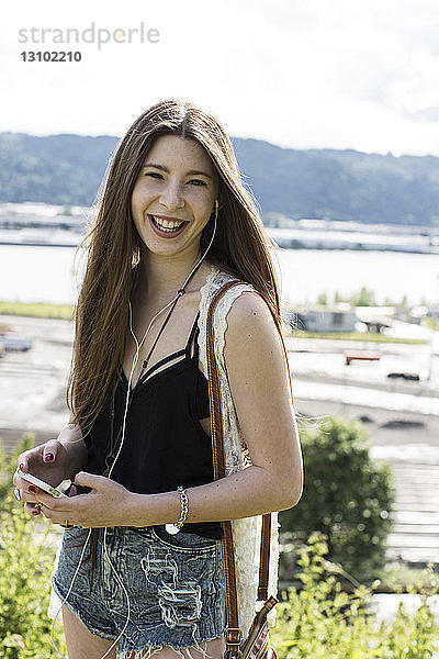 Porträt eines lächelnden Teenager-Mädchens  das auf dem Feld stehend Musik hört