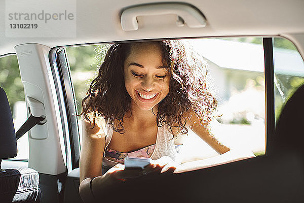 Lächelnde Frau benutzt Mobiltelefon  während sie sich ans Autofenster lehnt