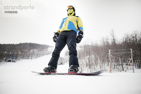 Niedrigwinkel-Ansicht eines auf einem Snowboard stehenden Mannes im Feld gegen den Himmel