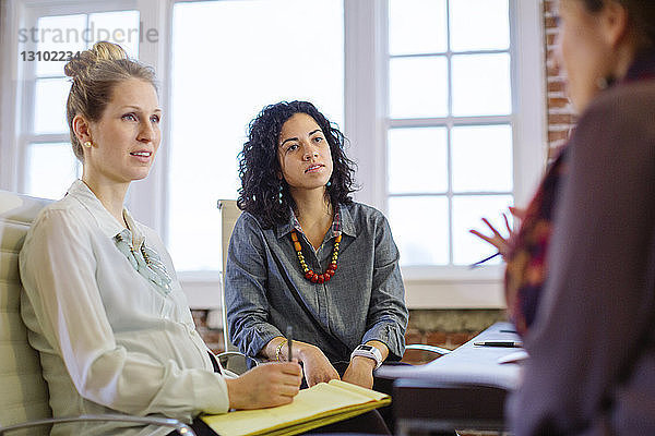 Weibliche Kollegen diskutieren  während sie im Büro am Schreibtisch sitzen