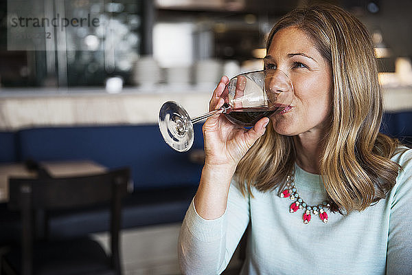 Glückliche Frau trinkt Rotwein im Restaurant