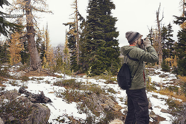 Mann fotografiert  während er im Winter im Wald steht