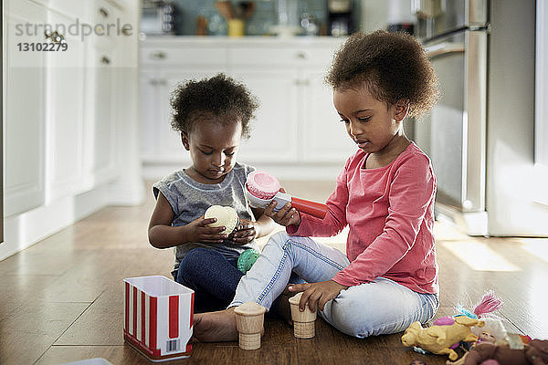 Schwestern spielen mit Eisspielzeug  während sie zu Hause in der Küche auf dem Hartholzboden sitzen