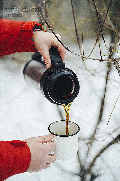 Geschnittene Hände einer Frau  die im Winter schwarzen Kaffee aus einem isolierten Getränkebehälter in einen Becher gießt