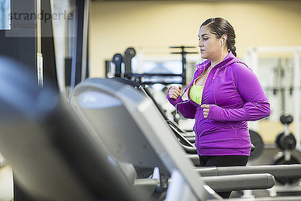 Frau hört Musik  während sie im Fitnessstudio auf dem Laufband joggt