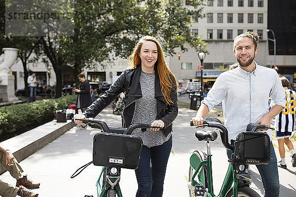 Glückliches Paar zu Fuß mit dem Fahrrad auf der Stadtstraße