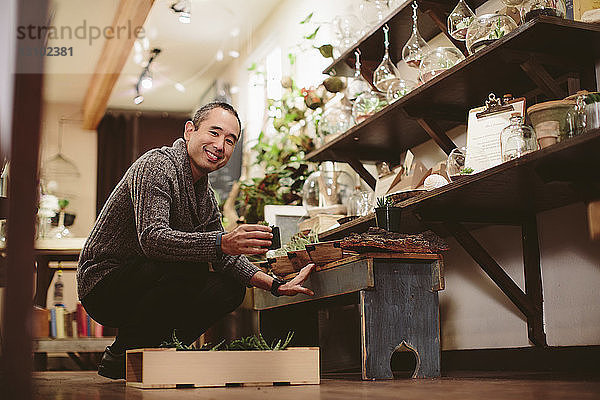 Porträt eines lächelnden Arbeiters  der im Geschäft Pflanzen auf dem Tisch arrangiert
