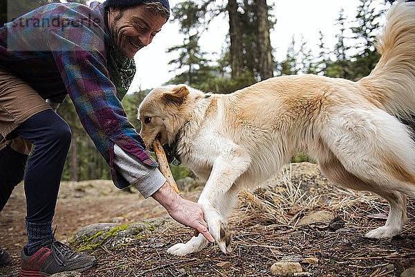 Glücklicher Mann spielt mit Hund im Wald