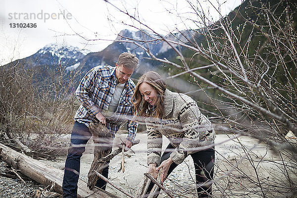 Junges Paar sammelt Holz für Lagerfeuer gegen Berge