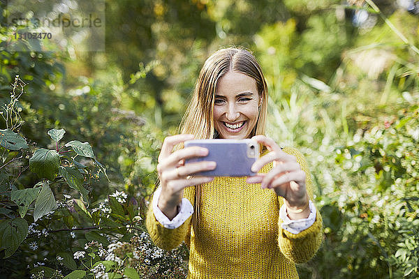 Fröhliche junge Frau fotografiert im Stehen inmitten von Pflanzen