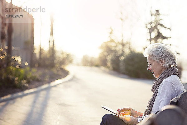 Ältere Frau mit Tablet-Computer auf Bank am Gehweg