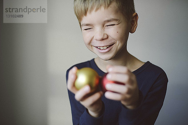 Fröhlicher Junge mit geschlossenen Augen hält Christmas Baubles zu Hause an die Wand