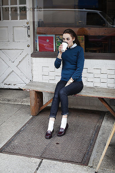 Frau sitzt auf Bank und trinkt Kaffee