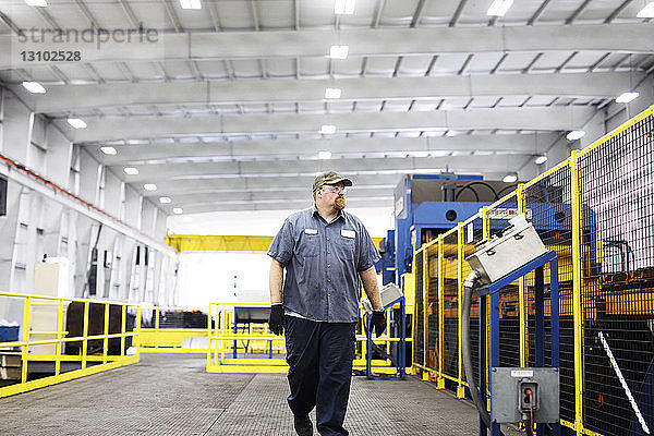 Selbstbewusster Arbeiter geht in voller Länge an Geräten in einer Fabrik der Metall-Stahlindustrie vorbei