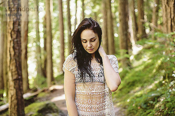 Frau mit Hand im Haar steht am Wald