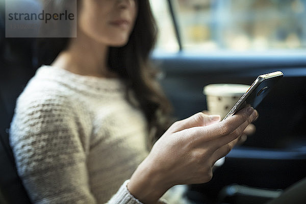 Mitschnitt einer Frau  die ein Smartphone benutzt  während sie im Taxi Einwegglas hält