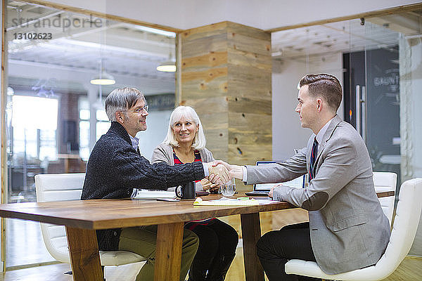 Geschäftsleute schütteln sich die Hand  während sie mit einer Kollegin im Büro sitzen