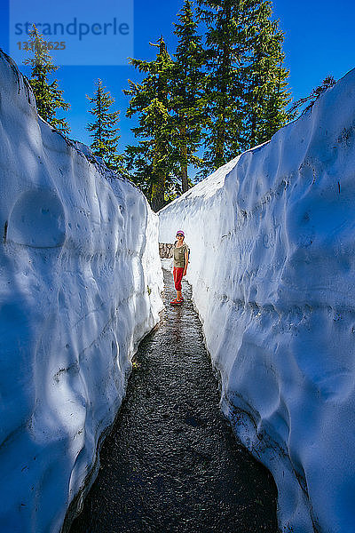 Ältere Frau steht in schmalem Gang inmitten von Eis im Crater Lake National Park