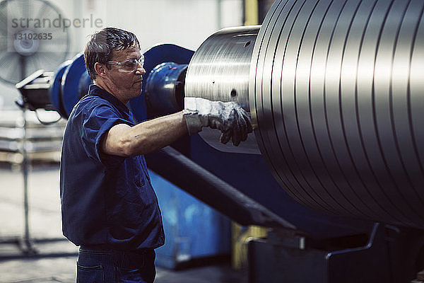 Älterer Arbeiter prüft in Stahlblechen  die auf einer Maschine in der Industrie rollen