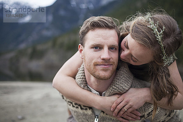 Porträt eines Freundes  während ihn seine Freundin gegen die Berge umarmt