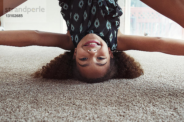 Porträt eines verspielten Mädchens beim Kopfstand auf dem Teppich zu Hause