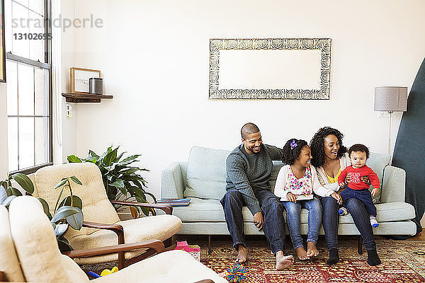 Glückliche Familie mit Bilderbuch  die den kleinen Jungen auf dem Sofa sitzend betrachtet
