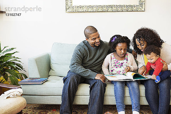 Familie schaut ins Bilderbuch  während sie auf dem Sofa sitzt