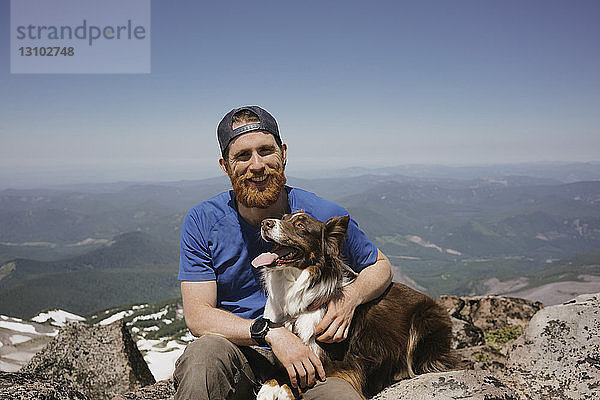 Porträt eines Mannes mit Hund auf Berg gegen Himmel sitzend