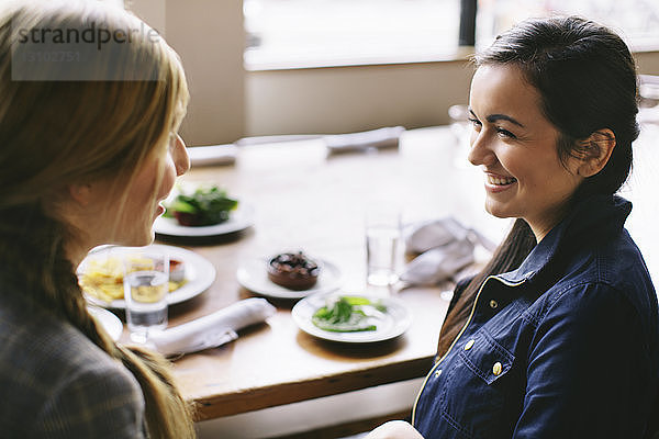 Schrägansicht auf glückliche Freundinnen  die sich unterhalten  während sie im Restaurant am Tisch sitzen