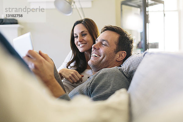 Glückliches Paar benutzt digitales Tablet  während es sich zu Hause auf dem Sofa entspannt
