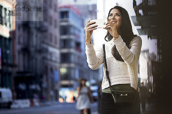 Glückliche Frau fotografiert durch Smartphone in der Stadt