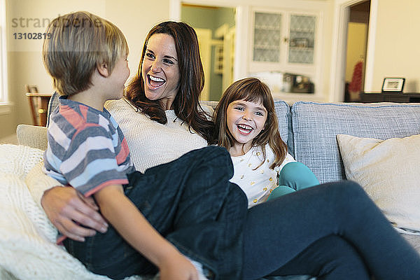 Fröhliche Mutter mit Kindern  die zu Hause auf dem Sofa sitzen