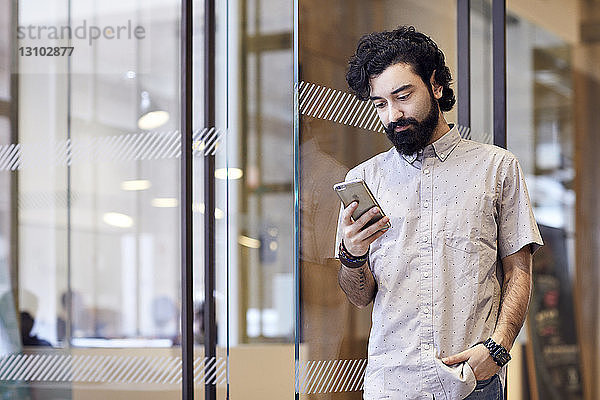 Geschäftsmann benutzt Smartphone  während er im Büro an der Tür steht