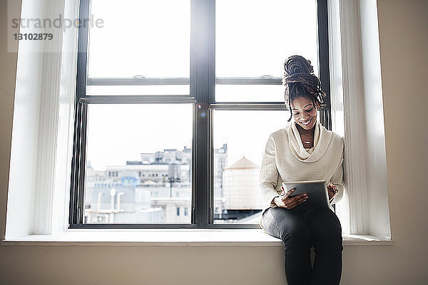 Lächelnde Geschäftsfrau benutzt digitales Tablet  während sie am Fenster sitzt