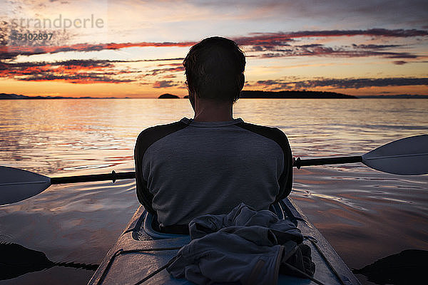 Rückansicht eines Mannes  der sich bei Sonnenuntergang im Kajak entspannt