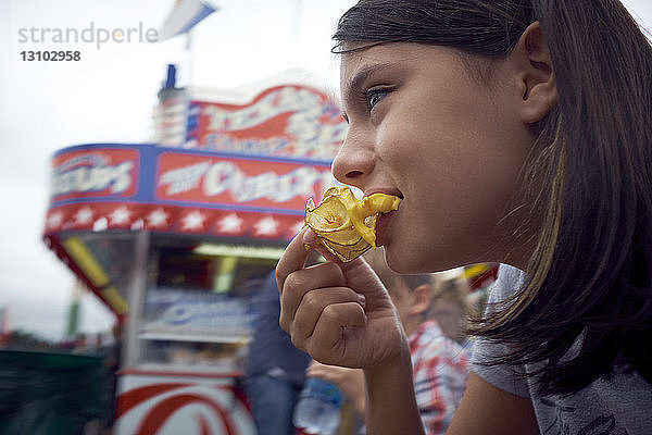 Niedrigwinkelansicht eines Mädchens  das Straßenessen isst  während es gegen den Himmel sitzt
