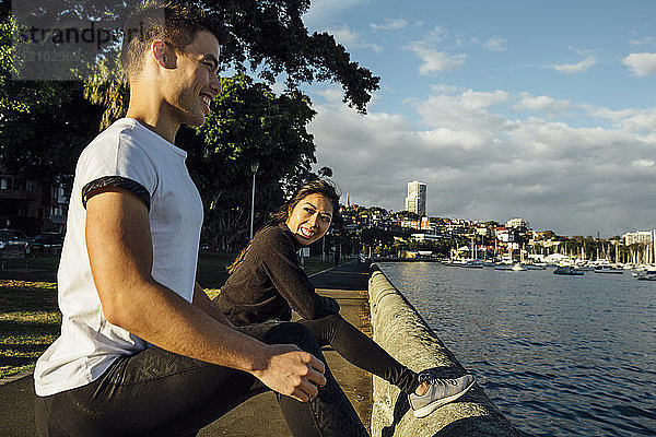 Glückliches junges Paar  das sich beim Training auf der Promenade vor bewölktem Himmel in der Stadt streckt