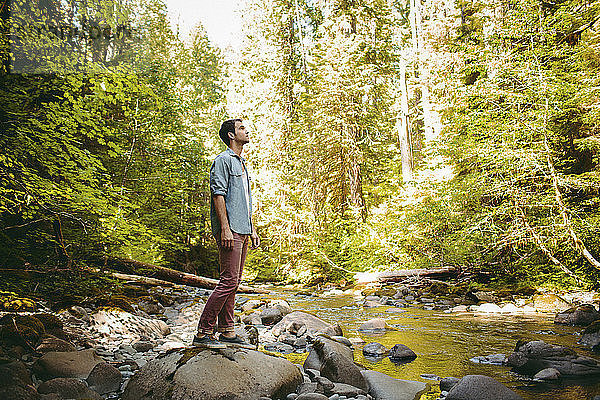 Mann in voller Länge auf einem Felsen am Fluss im Wald stehend