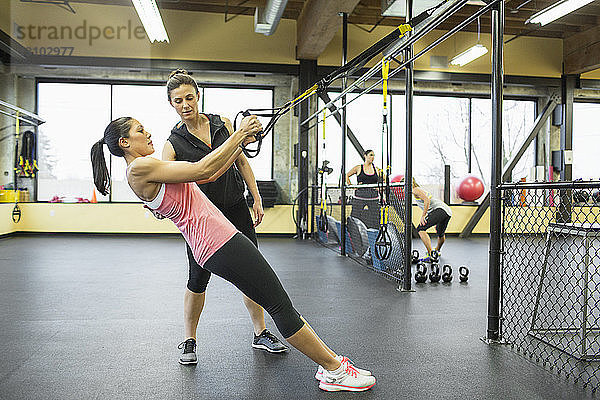 Ausbilderin  die einer Frau im Fitnessstudio beim Ziehen von Widerstandsbändern hilft