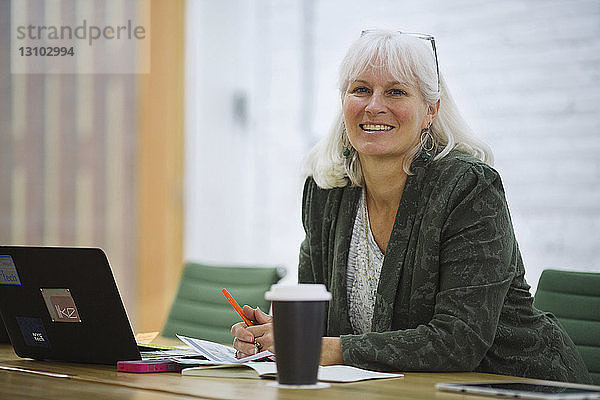 Porträt einer lächelnden Geschäftsfrau mit Laptop-Computer  die im Sitzungssaal im Büro sitzt