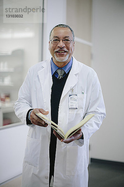 Porträt eines lächelnden männlichen Arztes mit Buch im Krankenhaus stehend