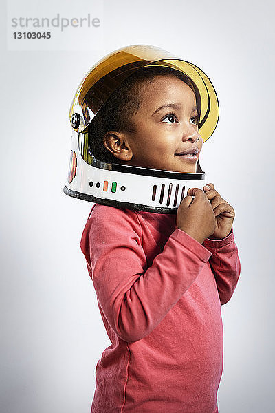 Nachdenkliches Mädchen mit Weltraumhelm beim Wegschauen vor weißem Hintergrund