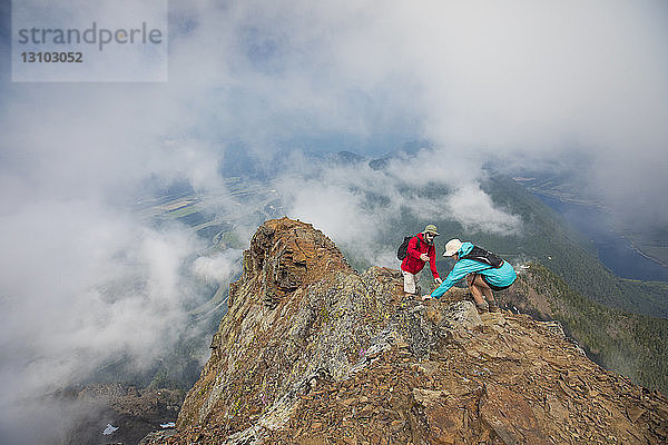 Hochwinkelaufnahme eines Wanderers  der einem Freund auf einem Berg inmitten von Wolken hilft