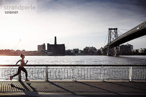 Entschlossene Frau joggt auf der Promenade mit der Williamsburg-Brücke im Hintergrund