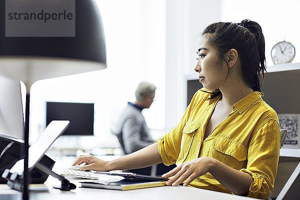 Geschäftsfrau  die am Desktop-Computer arbeitet  während ihr männlicher Kollege im Hintergrund sitzt