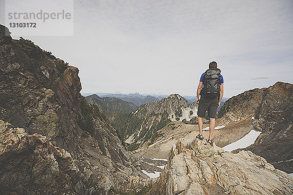 Wanderer mit Rucksack mit Blick auf die Aussicht  während er auf dem Berg gegen den Himmel steht