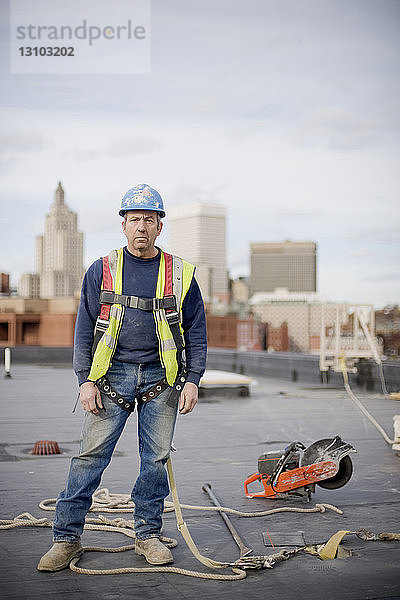 Porträt eines männlichen Arbeiters  der auf einem Gebäude auf einer Baustelle vor bewölktem Himmel steht
