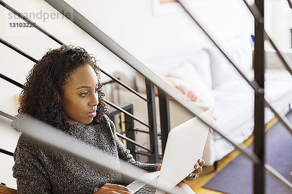 Frau benutzt Laptop-Computer  während sie zu Hause auf Stufen sitzt