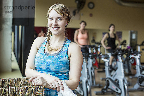 Porträt einer lächelnden Frau mit Freunden  die im Hintergrund im Fitnessstudio trainieren